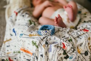 Baby's tiny feet rest on a whimsical patterned blanket with colorful doodles and a blue teething ring.