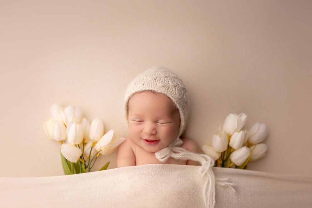 Sleeping baby with white bonnet surrounded by white tulips.