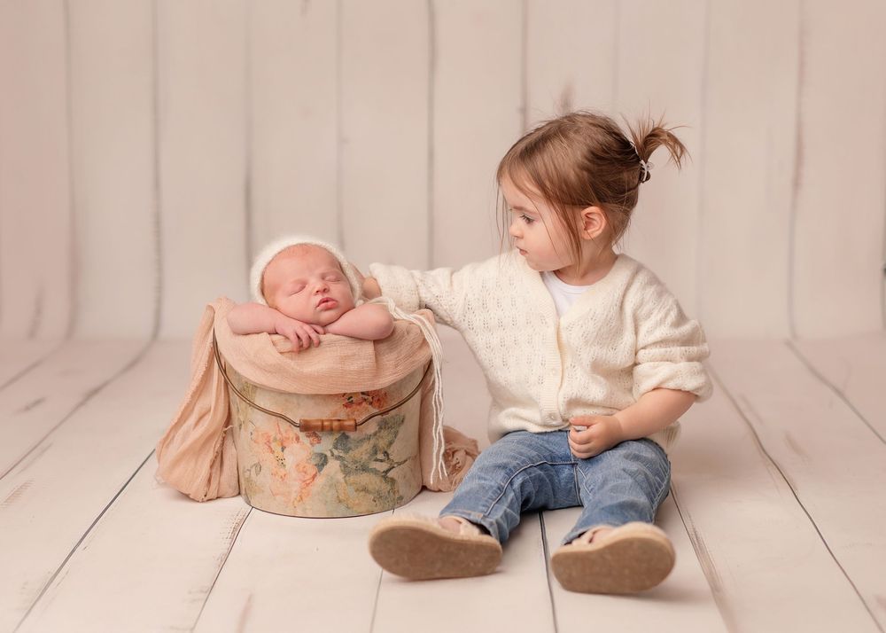 Newborn baby sleeping in a rustic bowl prop with casual denim pants on white wooden floor.
