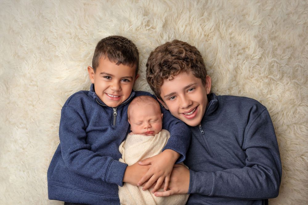 Three siblings posed together on cream colored fur backdrop for portrait.