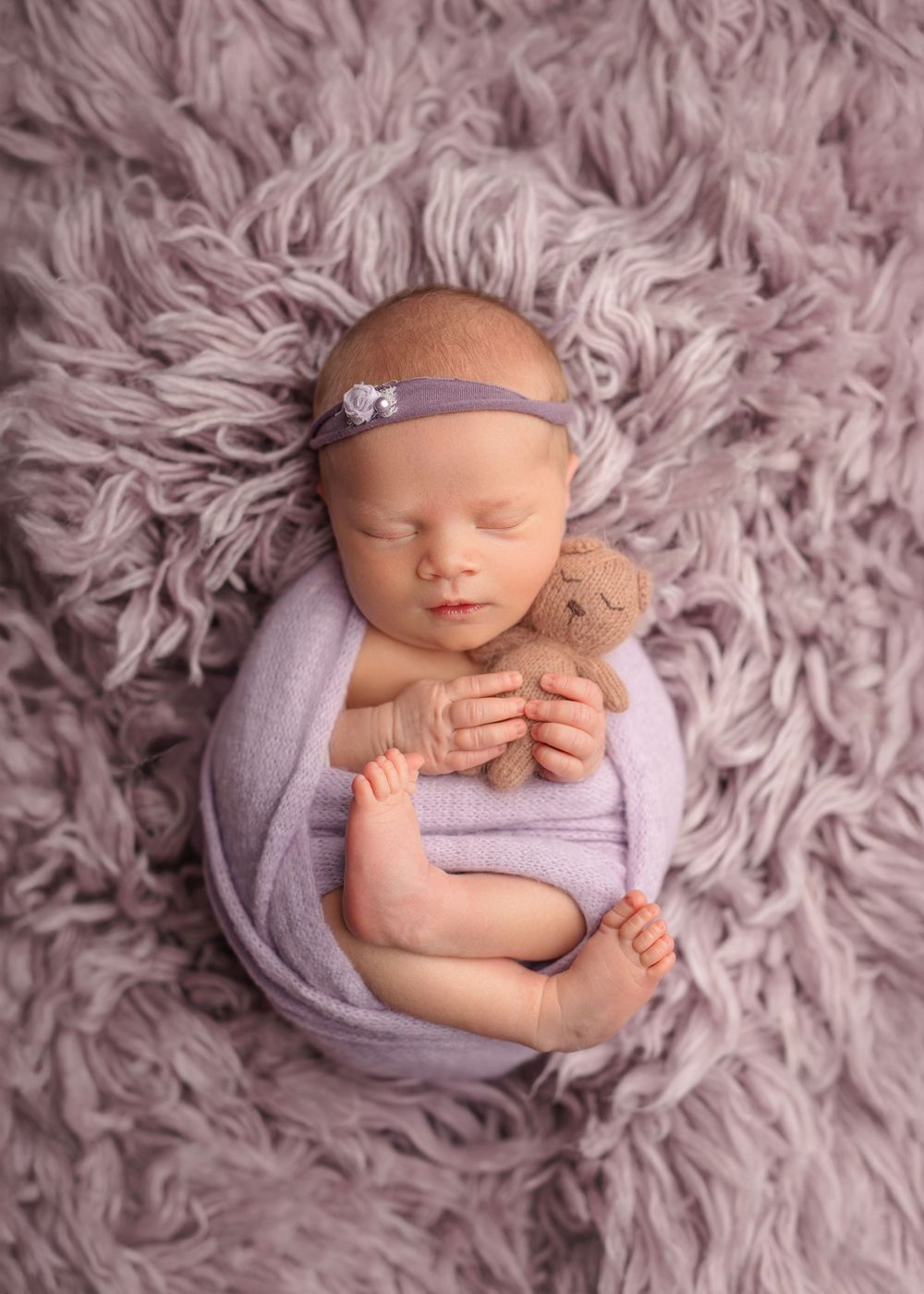 A sleeping newborn swaddled in lavender fabric lying on a plush gray fur blanket in a series of peaceful poses.