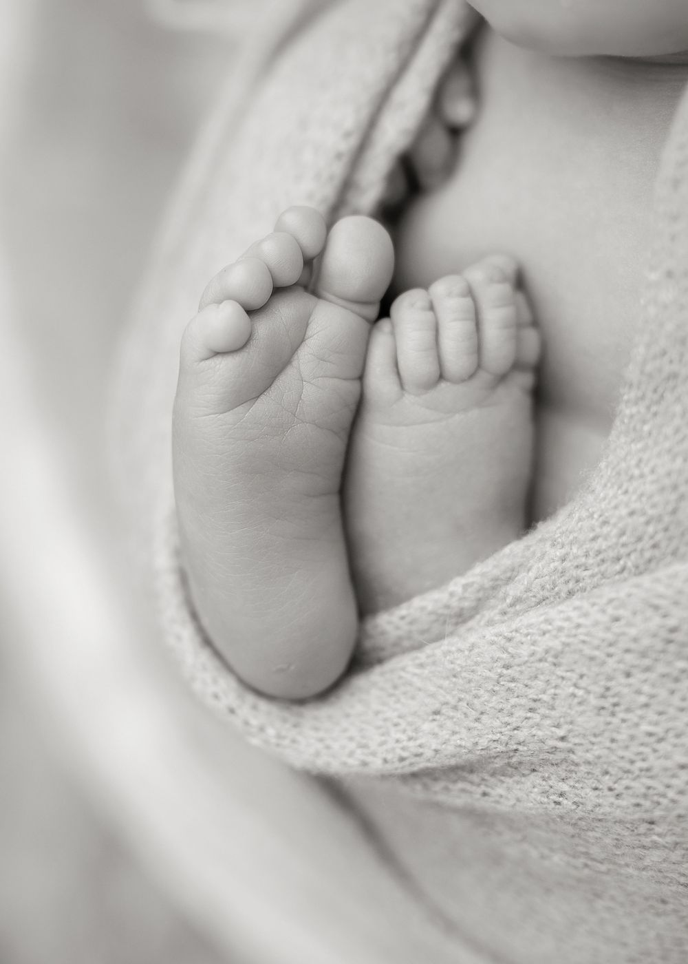 Close-up black and white photograph of tiny baby feet wrapped in soft knit blanket.