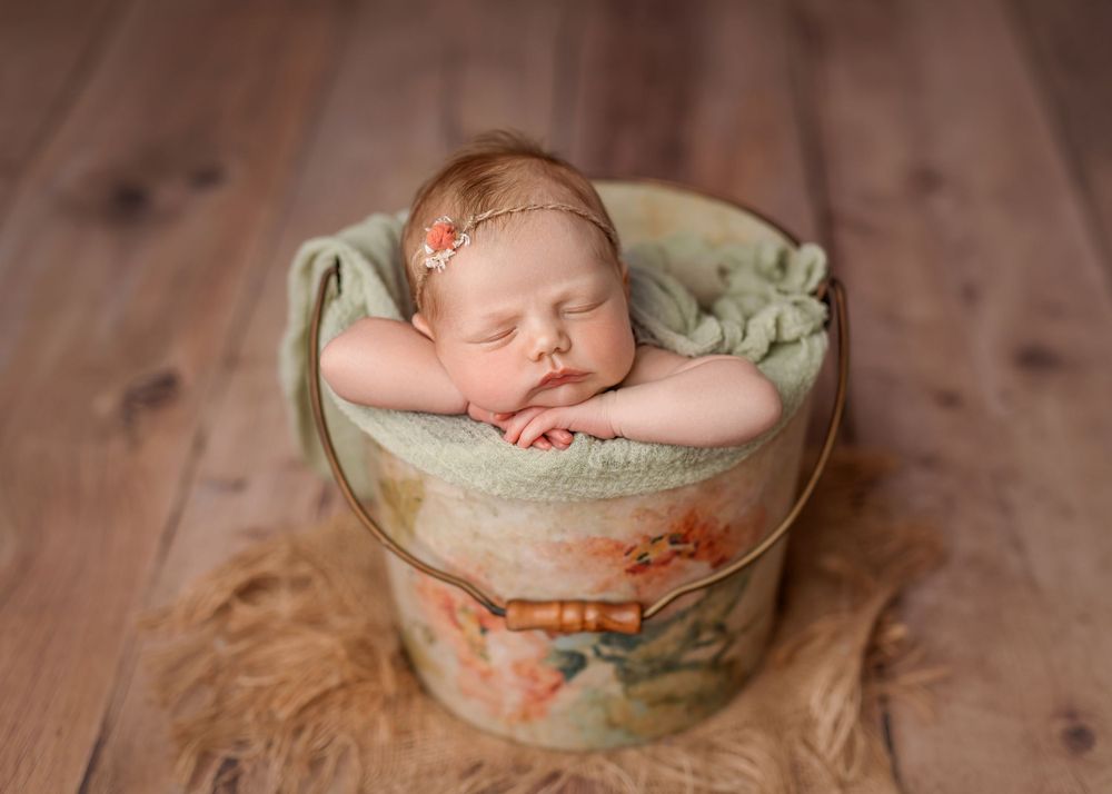 Peaceful newborn sleeps in vintage-style container on wooden surface with green wrapping.