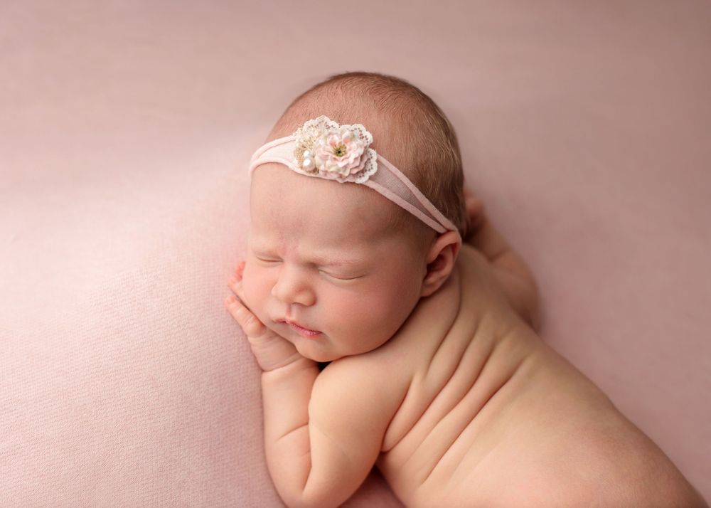 A peaceful newborn sleeping on a pink background in natural light.