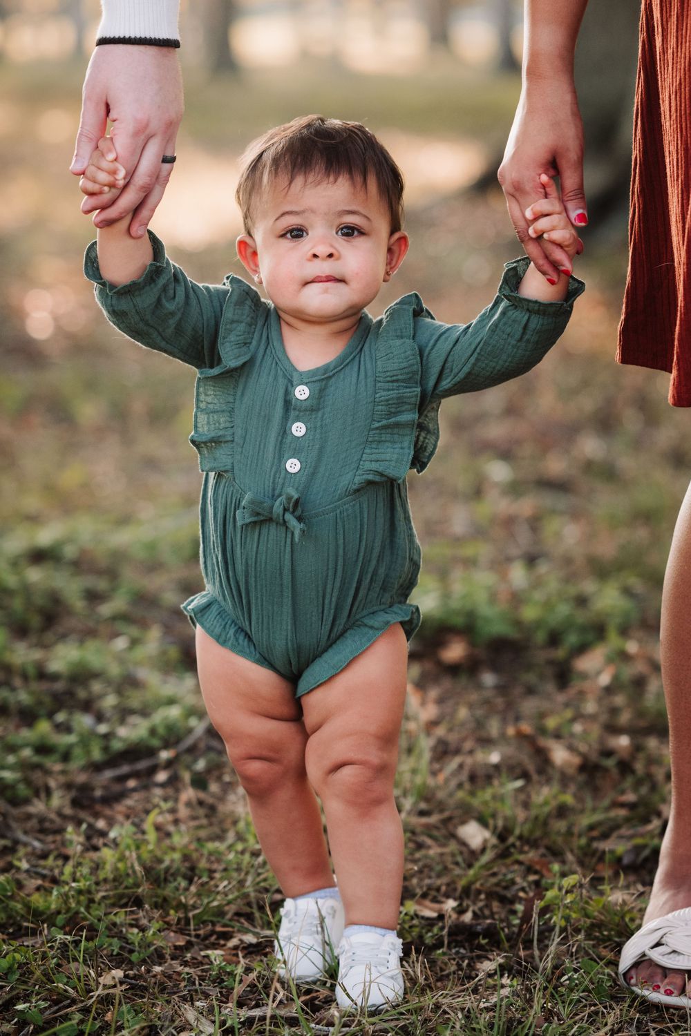 Baby in green romper taking first steps outdoors during autumn photo session.