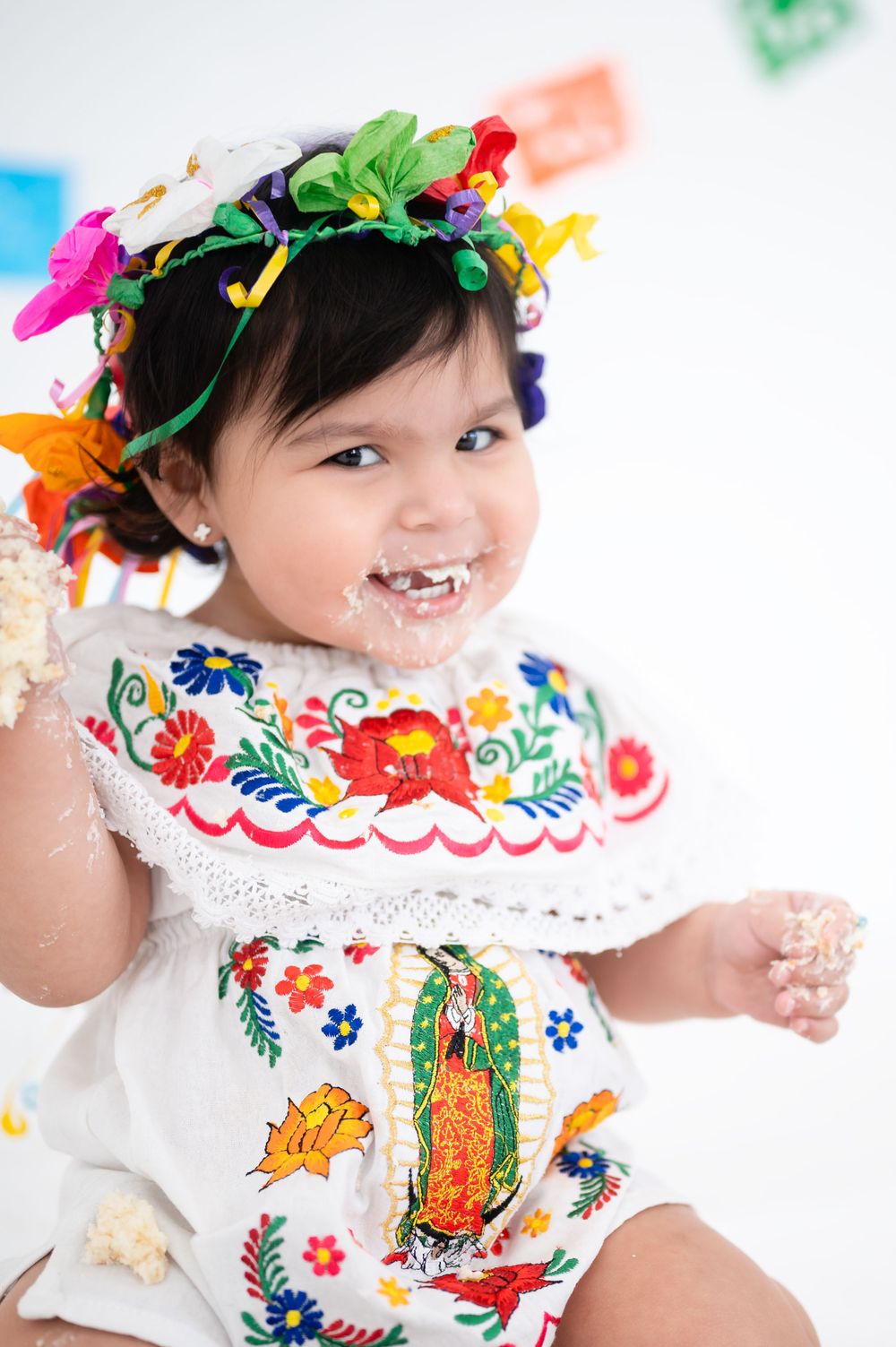 Baby wearing traditional embroidered dress with colorful flower crown.