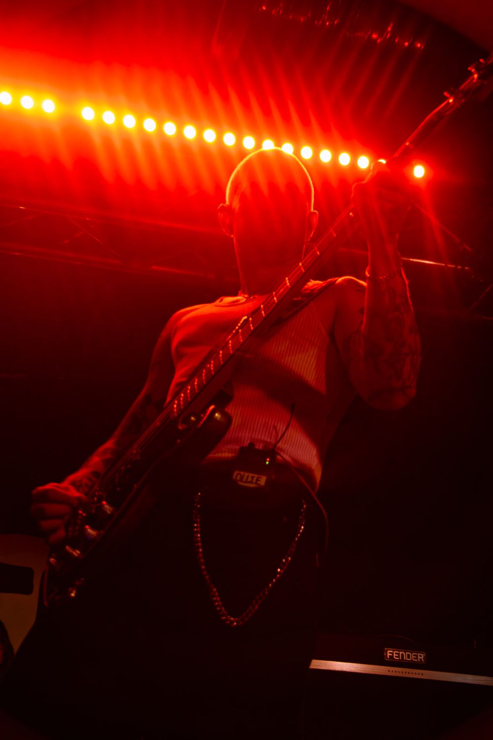 Multiple dark silhouettes performing on stage under dramatic red lighting with string instruments and spotlights.
