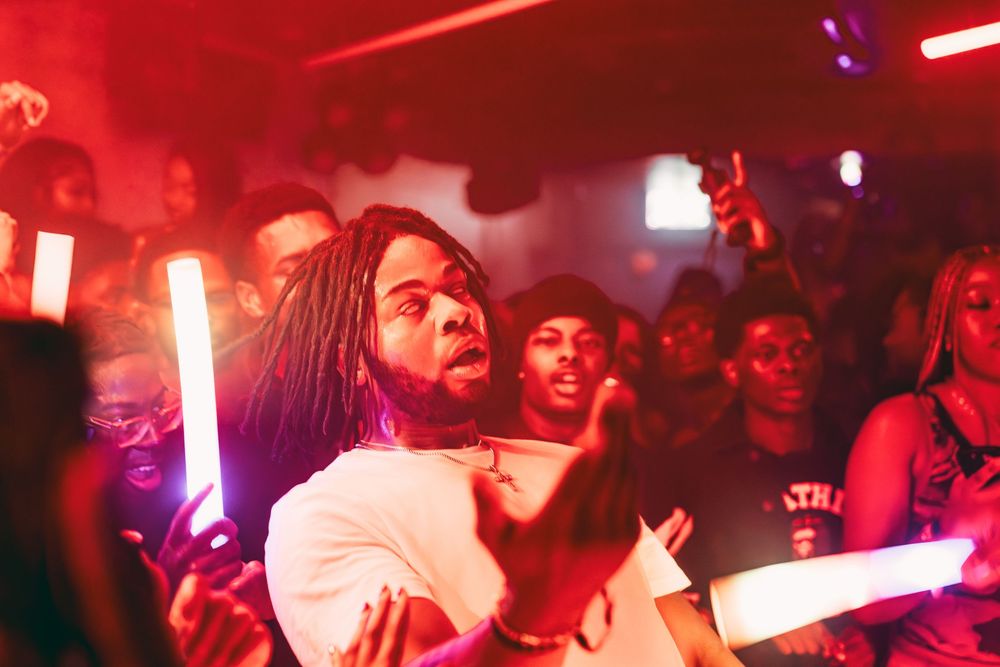 Crowd of people dancing in a nightclub illuminated by vibrant red lighting and neon effects.