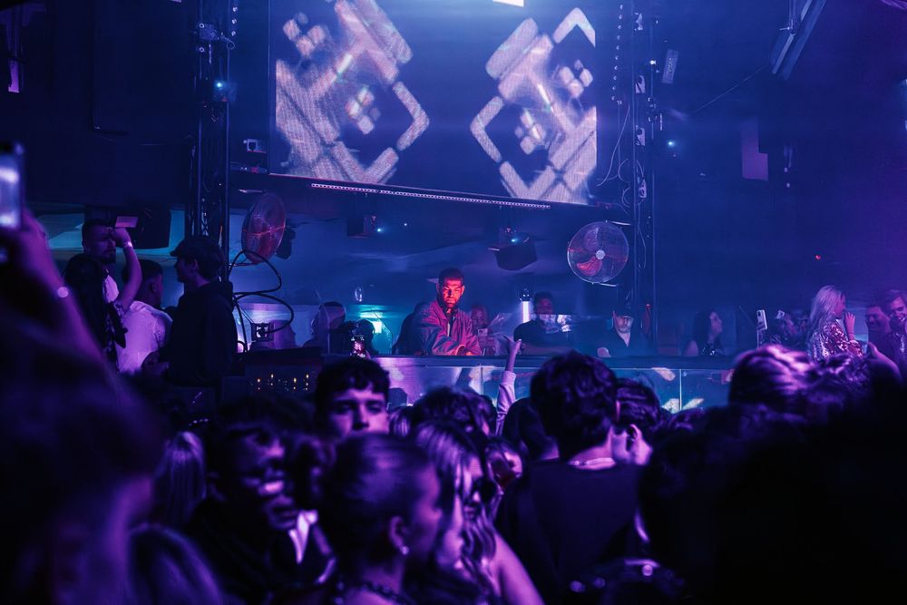 Concert crowd silhouettes enjoy vibrant purple lighting and stage effects at a nightclub performance.