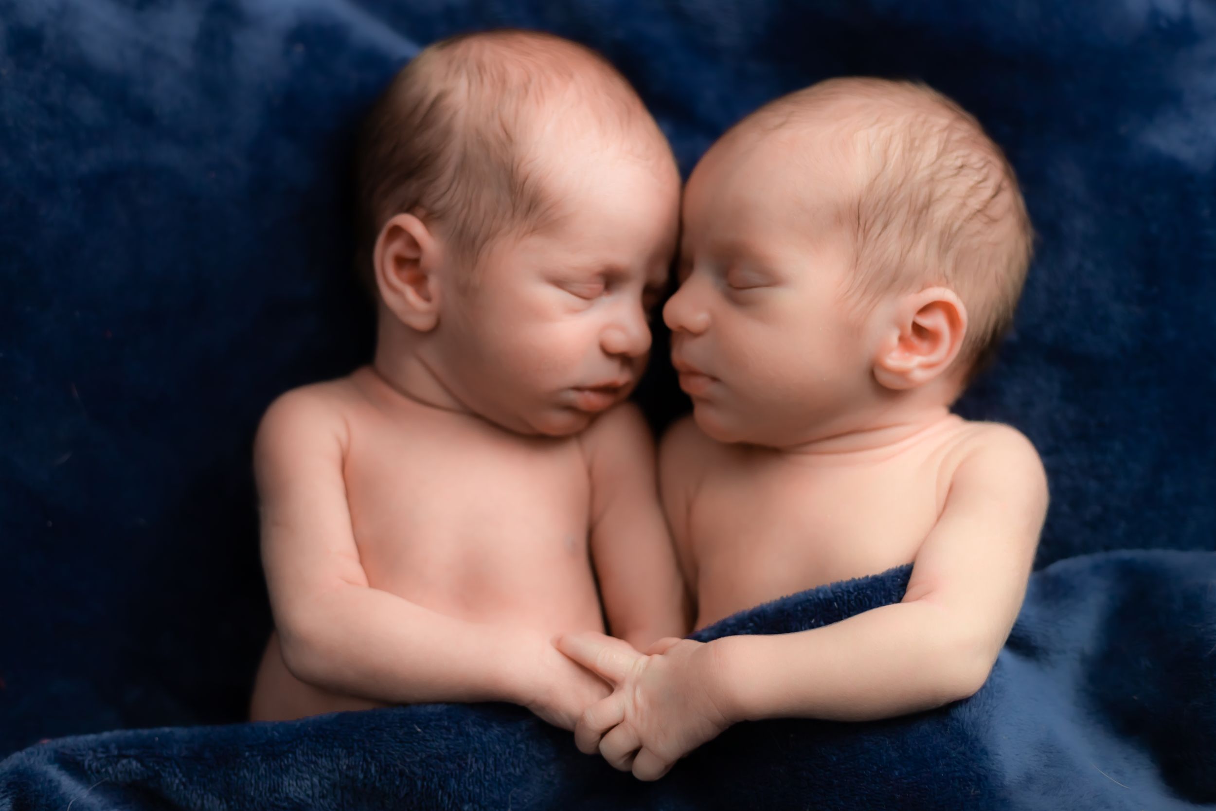 Two sleeping newborn babies lying close together on blue fabric.