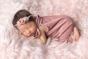 A sleeping baby wrapped in pink blankets lies peacefully on soft textured fabric.