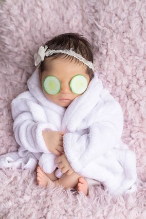 Spa-themed newborn photography series showing baby wrapped in white towel with cucumber slices and relaxation poses on pink blanket.