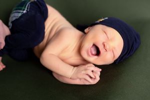 Sleeping newborn wearing navy blue hat on dark green background.