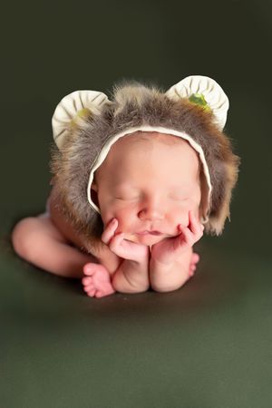 Newborn baby's feet wearing a white headband while sleeping on a dark green background.