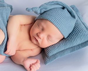 A baby's tiny feet wearing a soft blue knitted sweater rest peacefully on a white background.