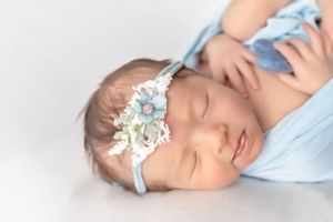 Peaceful newborn portrait with blue floral headband and wrapped in soft fabric.
