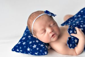Sleeping newborn with blue bow headband resting on star-patterned pillow.