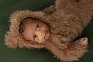 A baby wearing a fuzzy brown bear costume lies on a green blanket.
