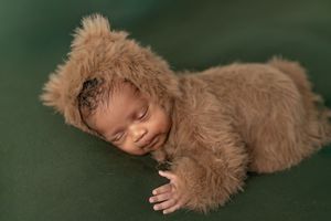 A sleeping baby wrapped in brown fur blanket lying on a green background in a professional newborn photo shoot.