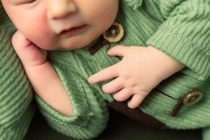 Small hands resting on a cozy green knit cardigan with wooden buttons.