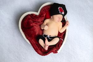 A series of five sequential photos showing a sleeping newborn baby nestled in a red heart-shaped cushion.