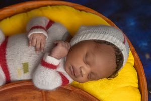 A baby sleeps peacefully in a yellow blanket while holding a white stuffed animal toy.
