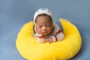 A series of photos showing a sleeping baby in a yellow crescent moon-shaped cushion against a blue backdrop.