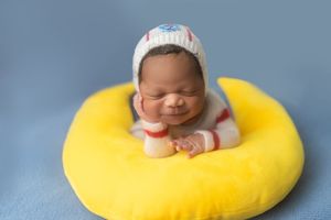 Newborn baby sleeping peacefully on a bright yellow circular support cushion.