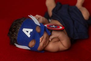 A superhero-themed photo series showing a sleeping baby in a Captain America costume on a red background.