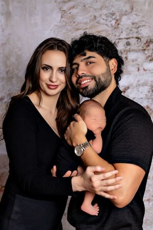Intimate family portrait with newborn baby against textured brick wall background.