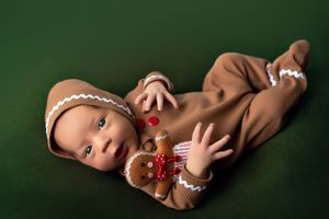 Baby in adorable gingerbread costume lying on dark green background.