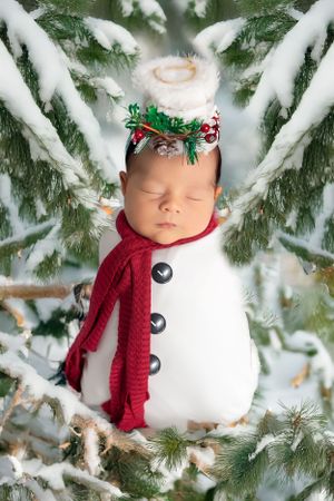 Creative newborn photo styled as cute snowman with red scarf and holiday decorations.