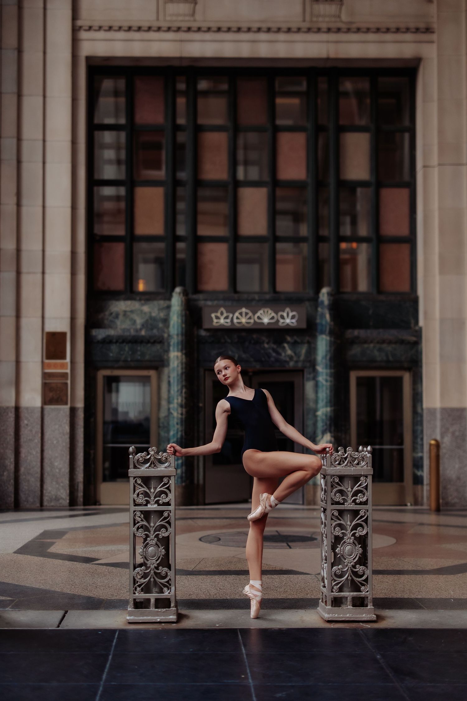 Ballet dancer poses gracefully between ornate iron posts in front of historic building entrance.