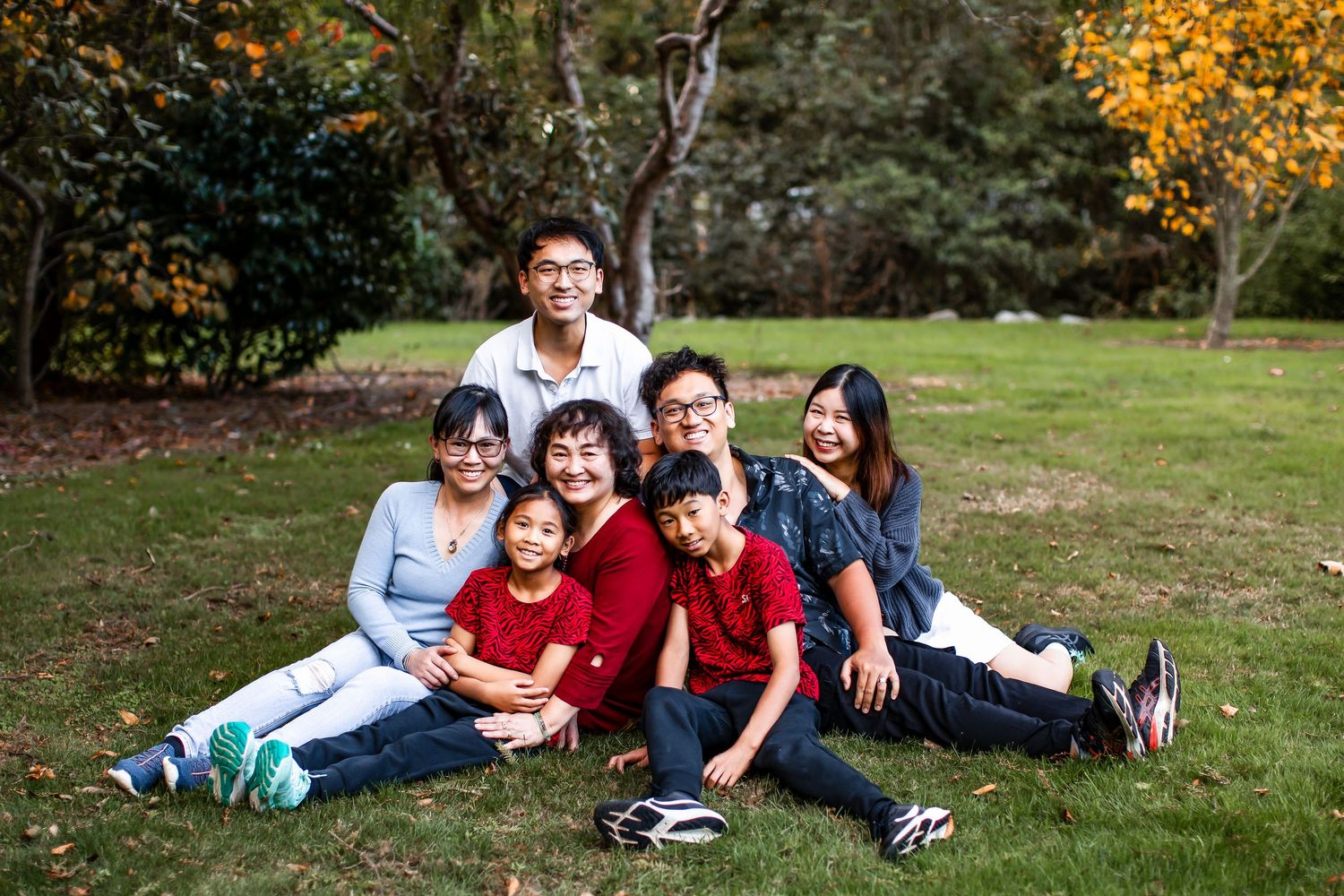 Group of people in casual clothing lying on green grass in a Palmerston North park during autumn.