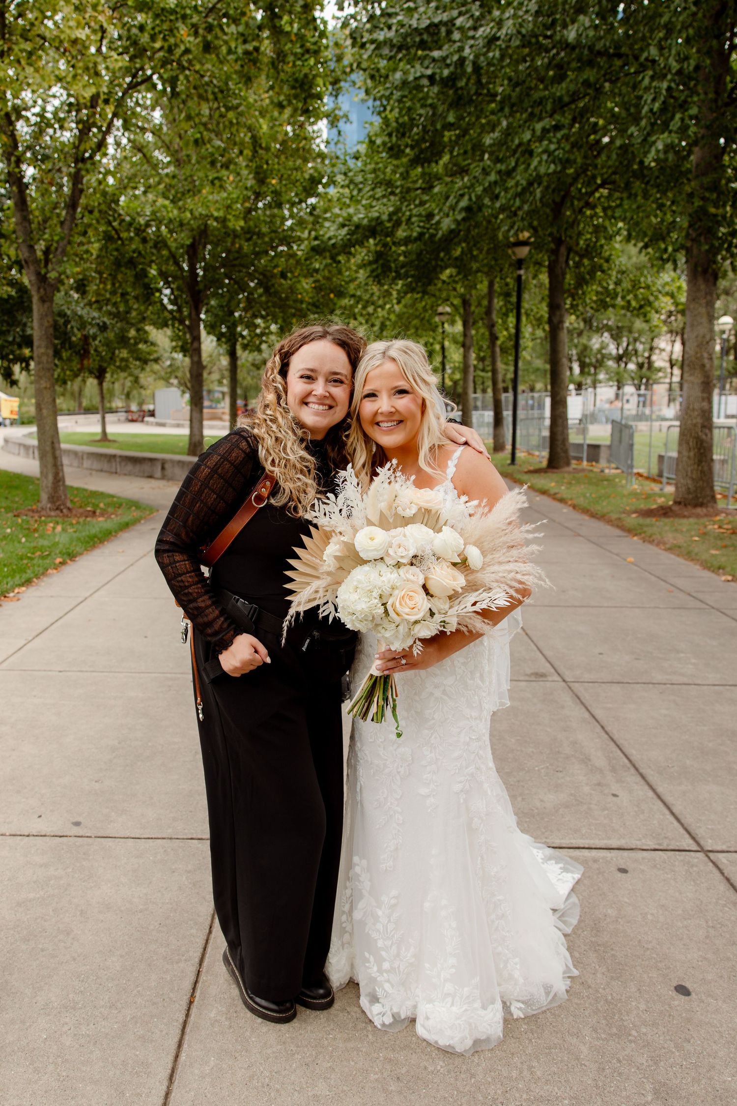 Wedding celebration on a tree-lined path with white bouquet and formal attire.