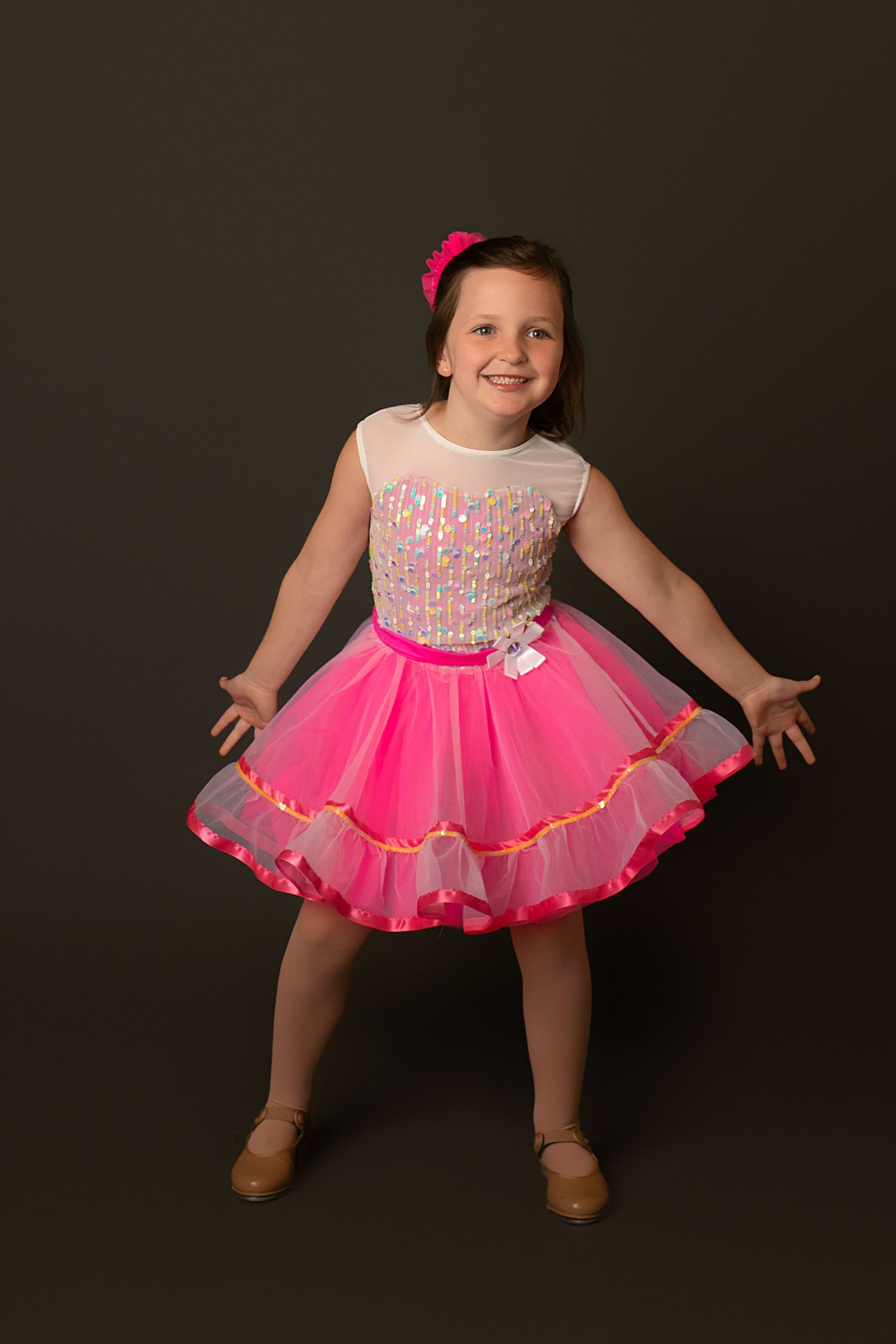 Dancer poses in pink tutu dress with sequined bodice against dark studio background.
