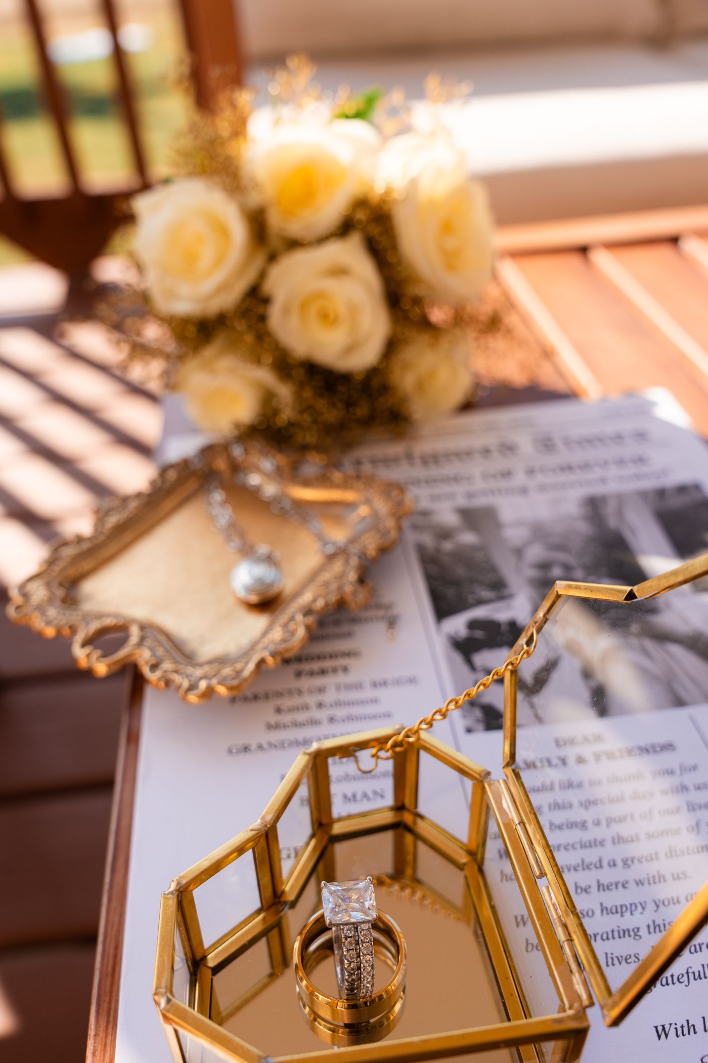 Wedding rings displayed in a gold geometric box with white roses and vintage photos in soft natural lighting.