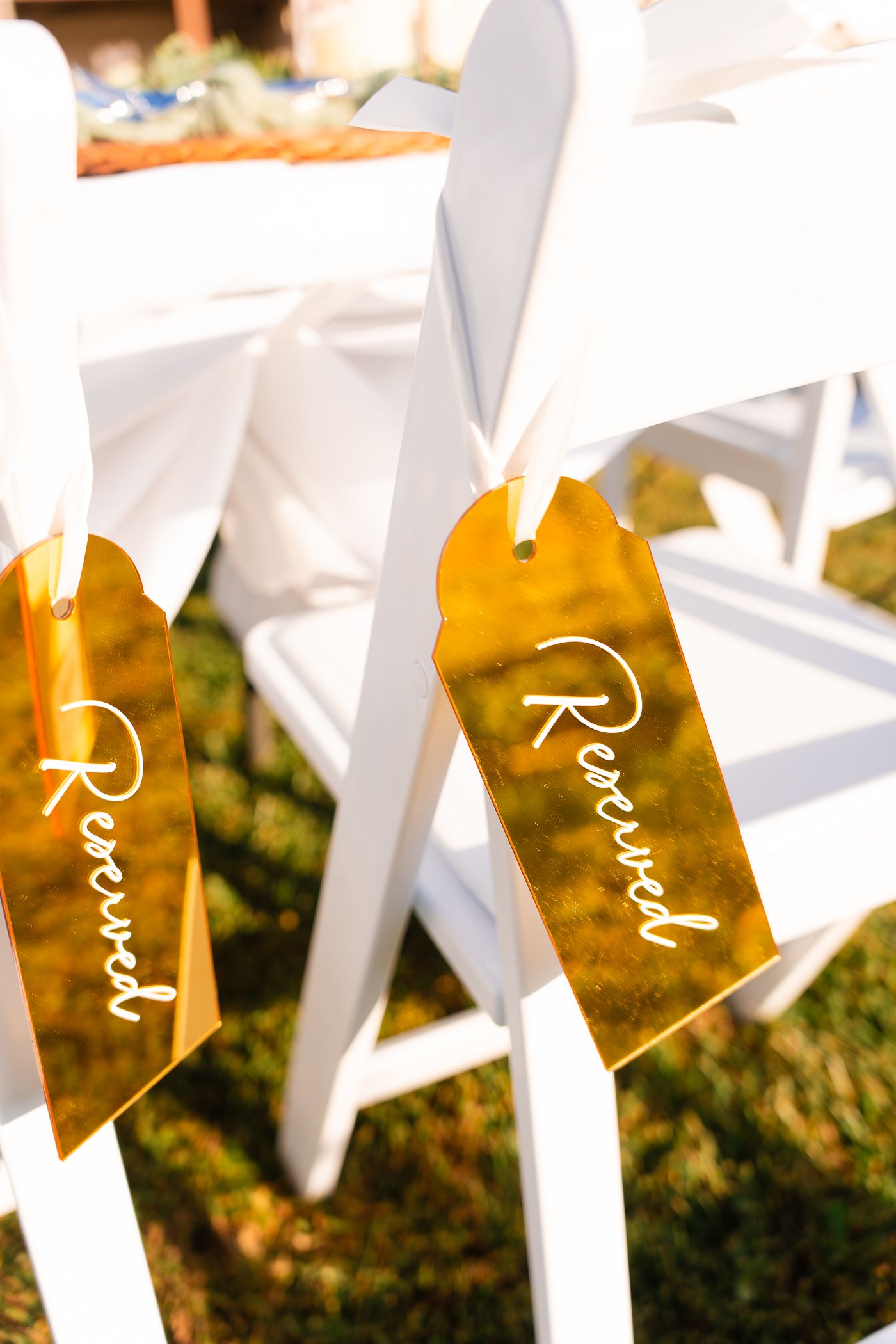 Row of white wedding ceremony chairs with name tags against a golden autumn background.