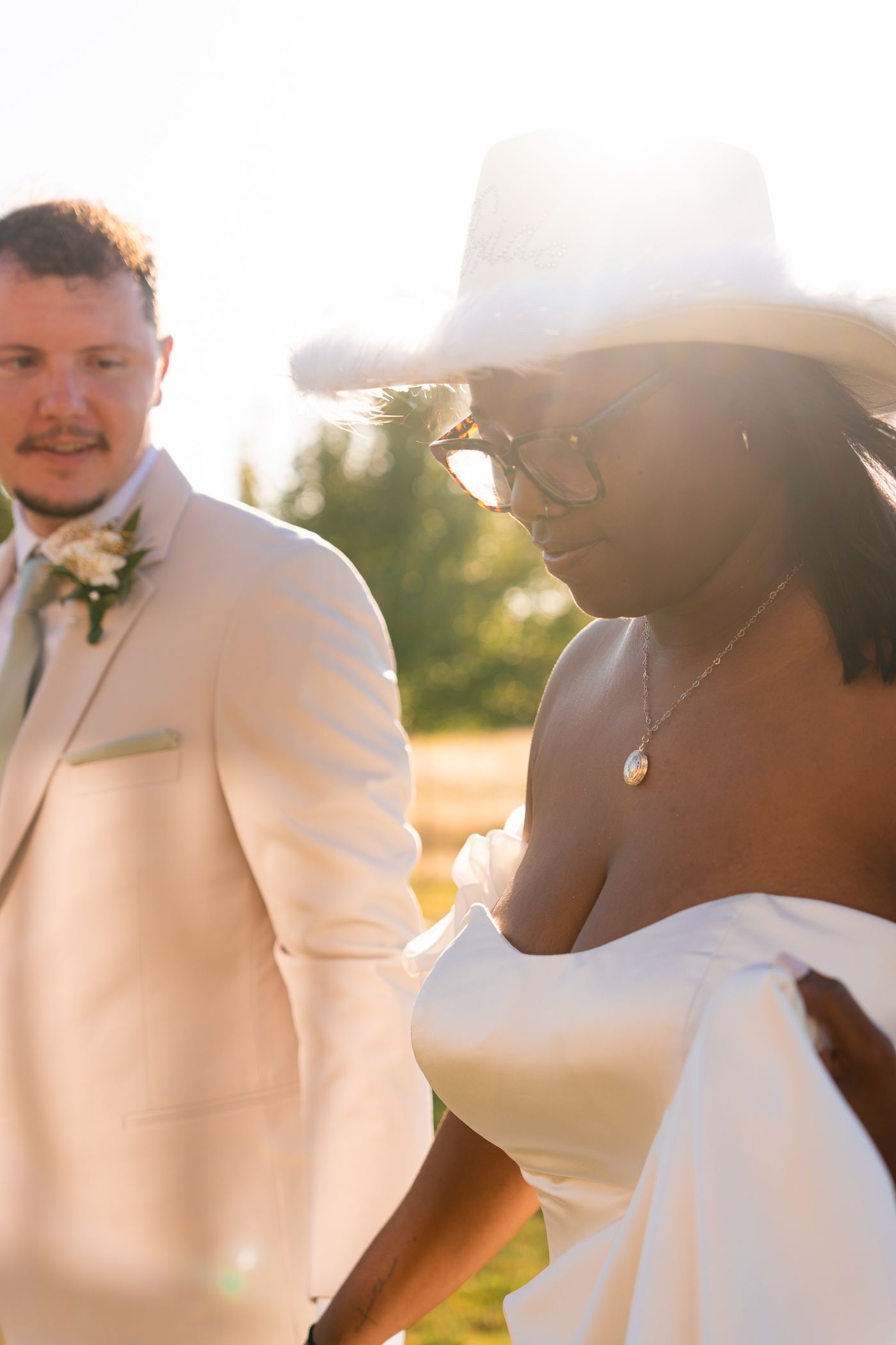 Wedding party in white suits and dresses pose together outdoors in golden sunlight.