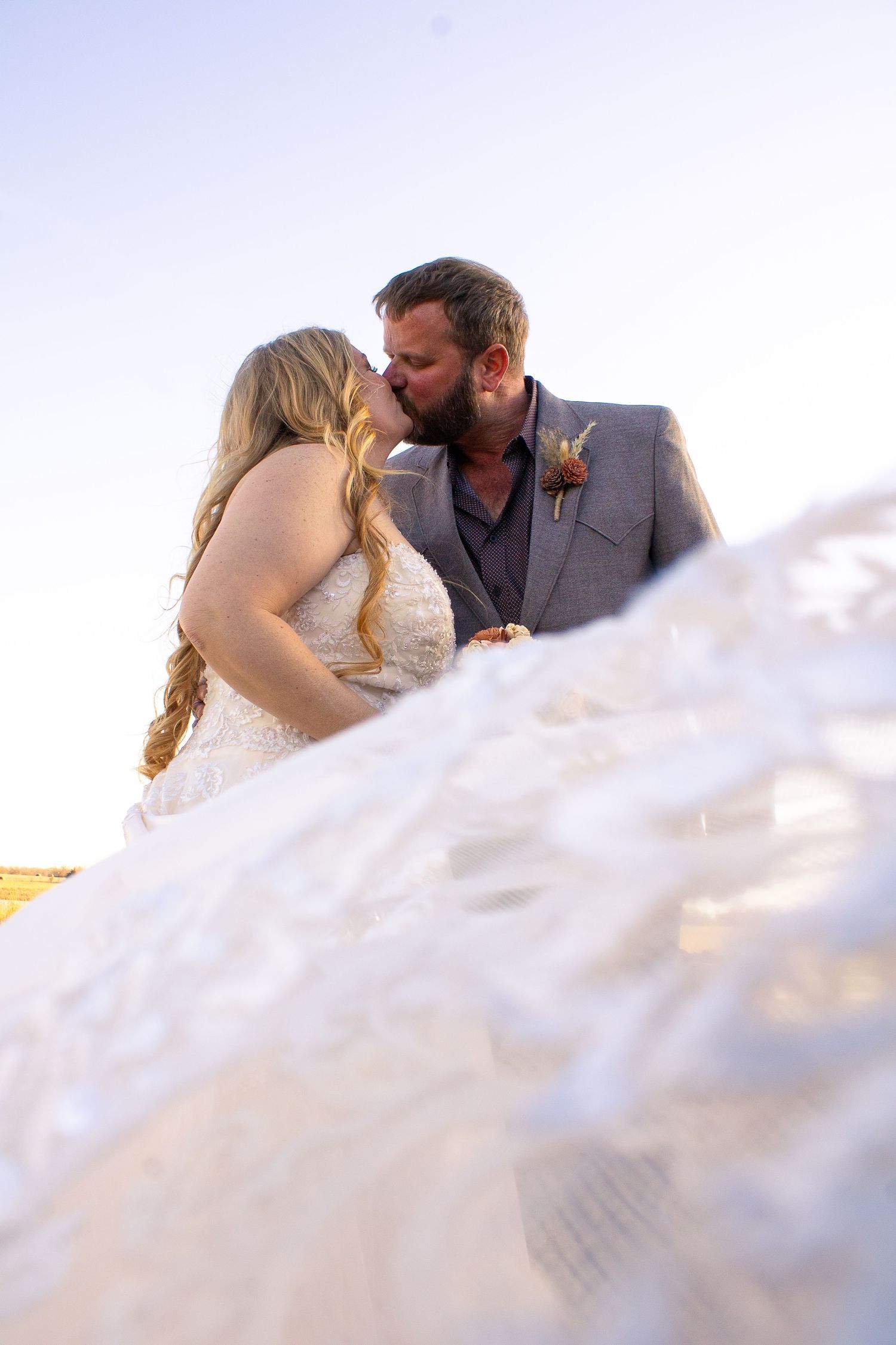 Romantic wedding couple embraces in soft sunlight with flowing white veil creating a dreamy atmosphere.