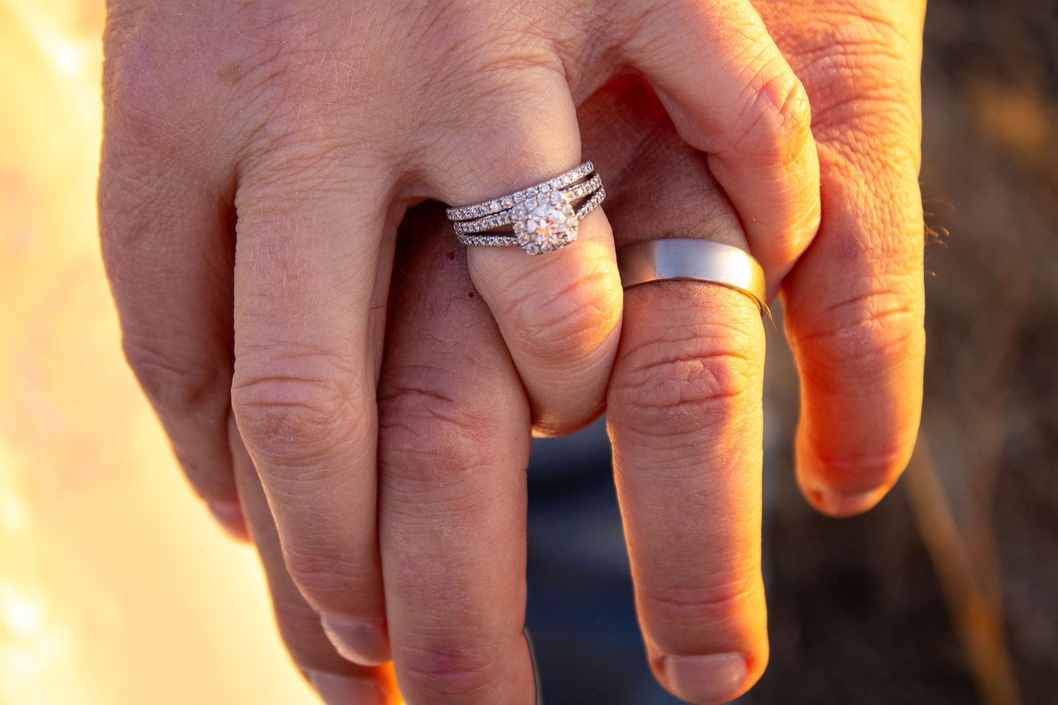 Close-up of wedding rings on hands in warm golden sunlight.