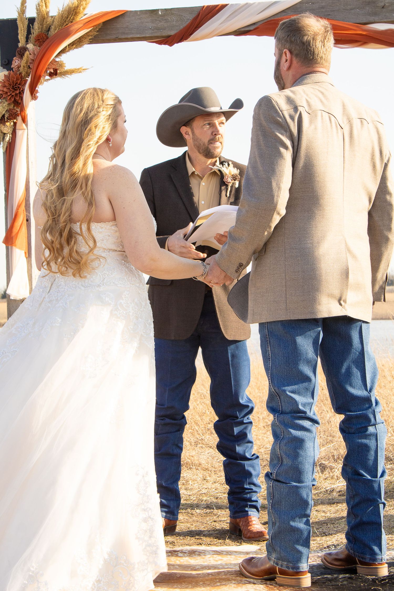 Wedding ceremony participants lined up outdoors with wheat stalks in background.
