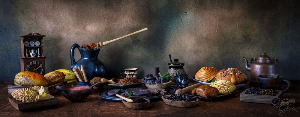 Dark and moody food photography setup with rustic plates, tea set, and pastries on wooden table in dim lighting.