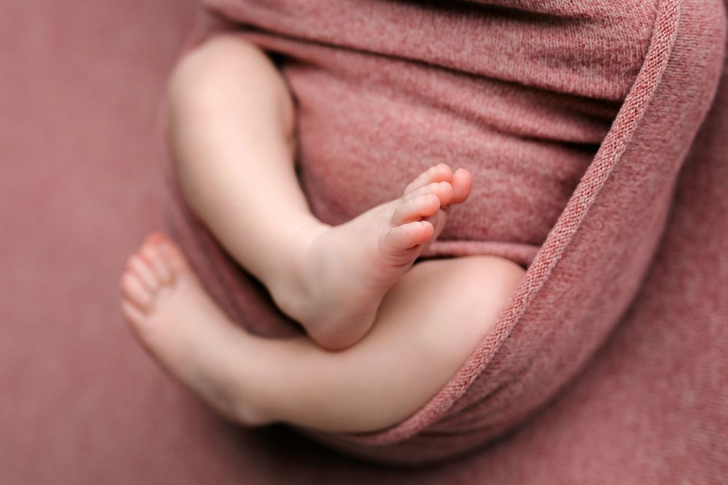 Newborn baby wrapped in dusty rose colored fabric for professional photography session.