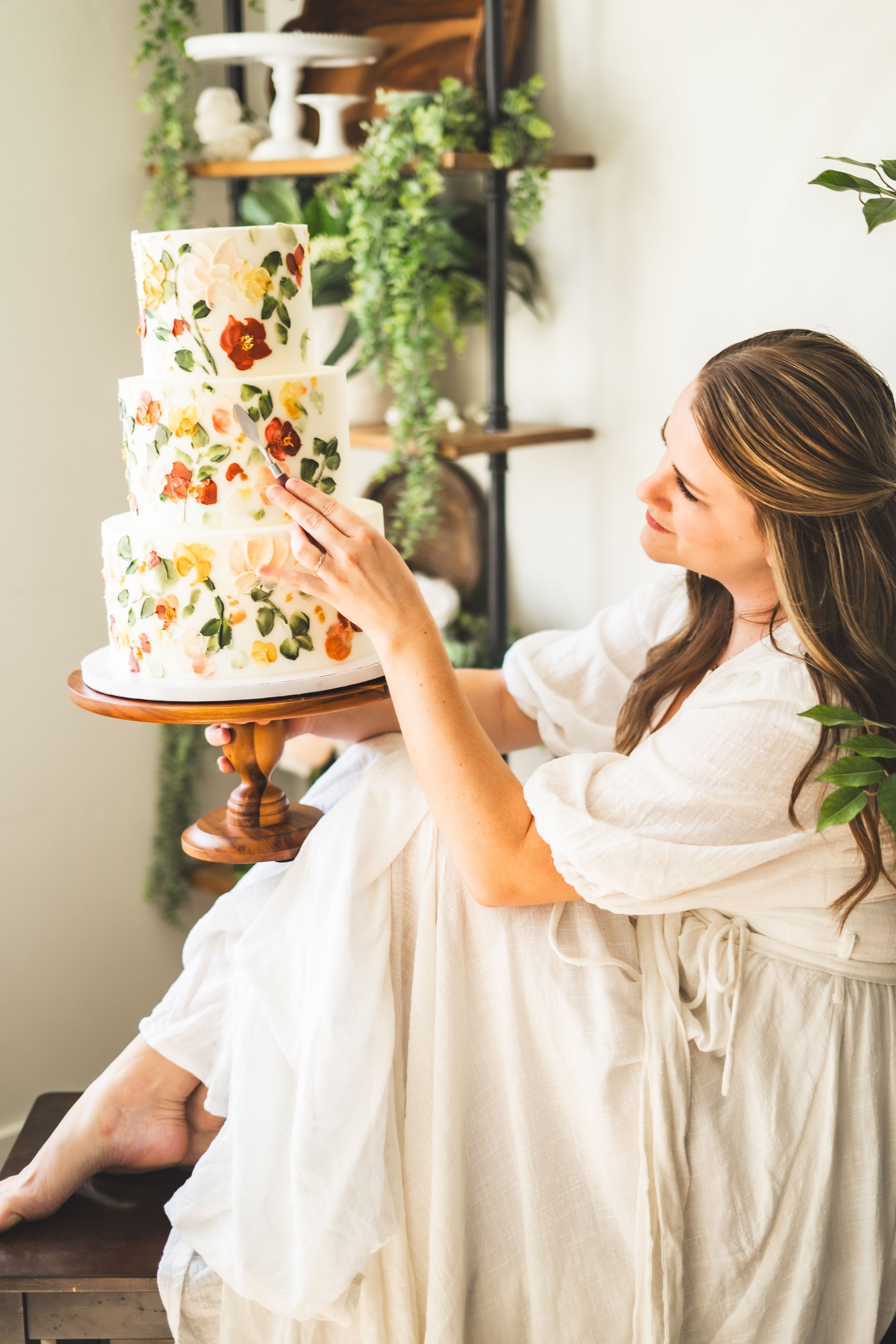 Baker in white dress arranging floral details on an elegant wedding cake.