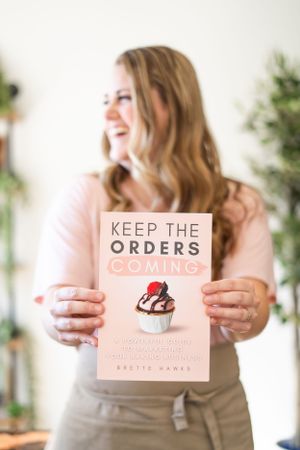 Book titled 'Keep the Orders Coming' being held up against white background with greenery.