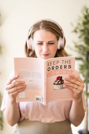 Reader wearing headphones while enjoying a book with pink cover.