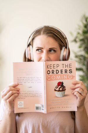 Close-up of book author wearing white headphones holding pink-covered book.