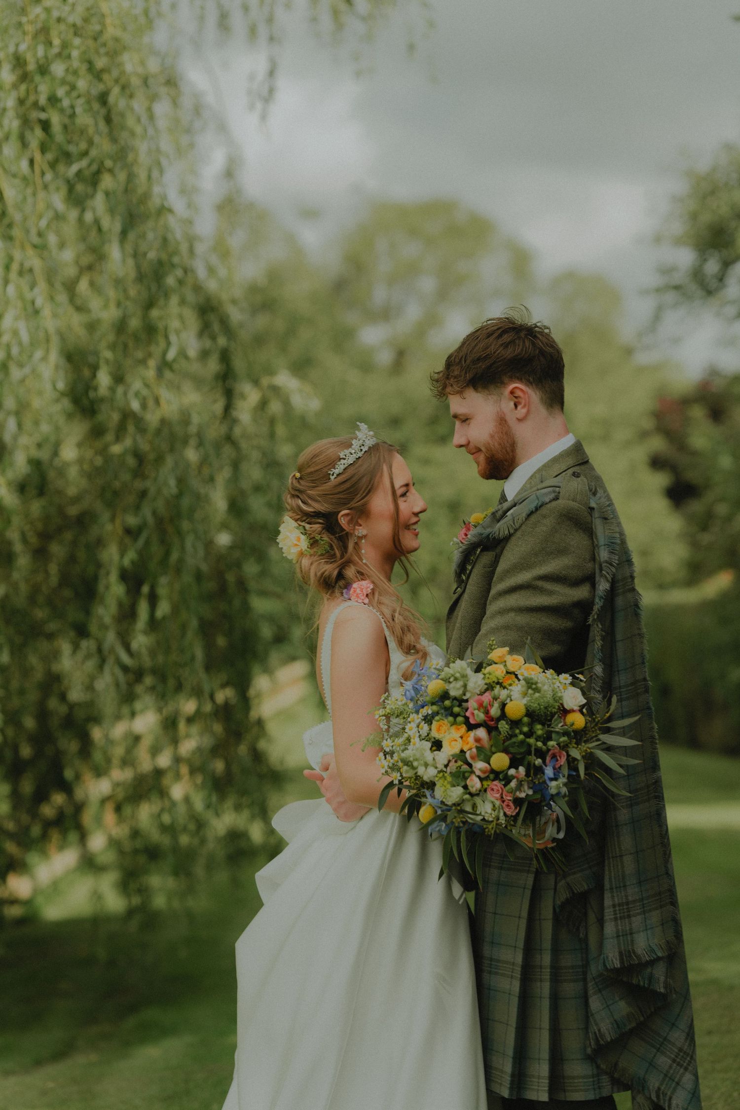 A couple poses playfully in front of blooming white flowers during their wedding.