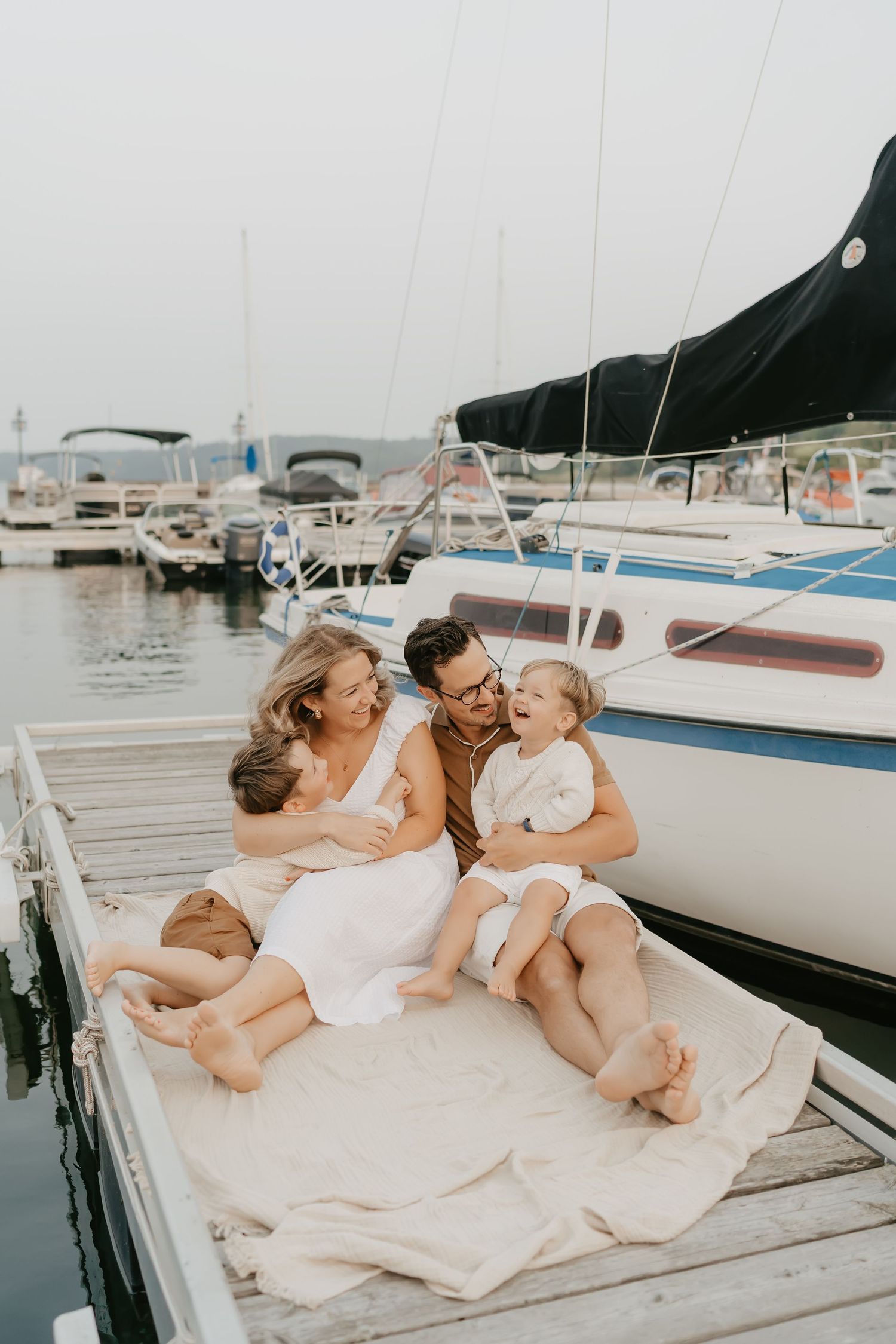 Family sharing intimate moment together while sitting on dock near boats at marina.